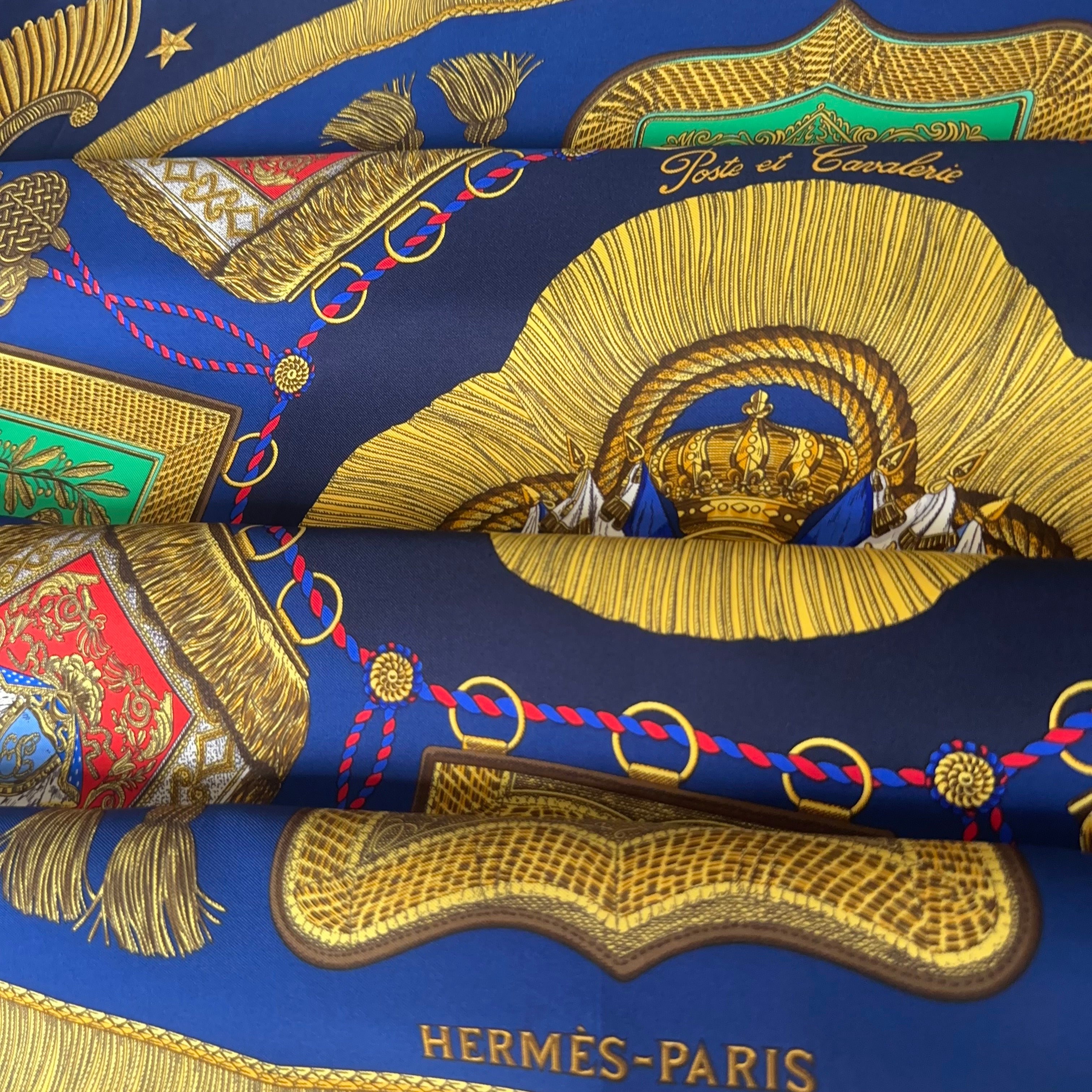 Le foulard plié artistiquement, mettant en valeur le contraste chic entre le bleu marine profond, le vert vif et l'or brillant.