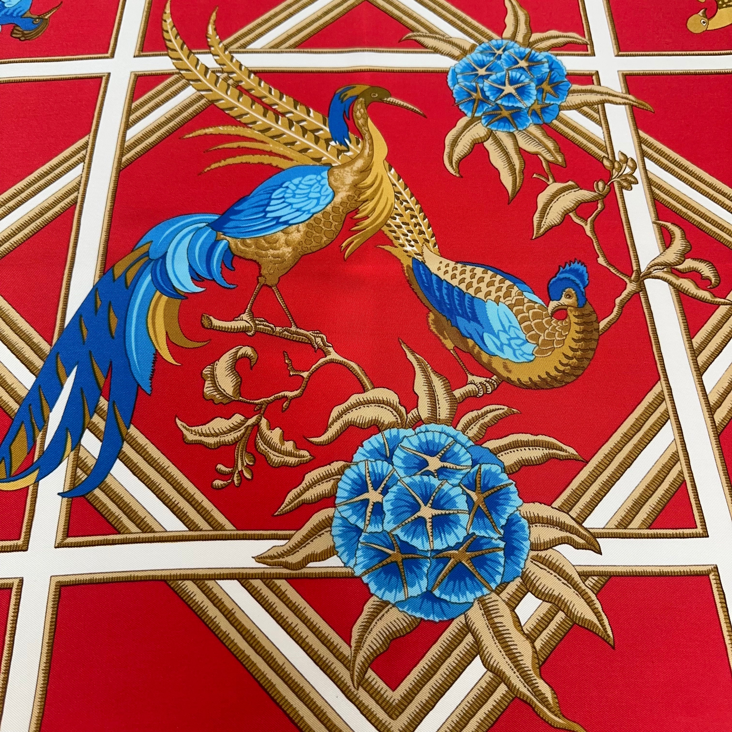 Gros plan central : deux oiseaux de paradis aux longues plumes bleues posés sur le treillage blanc, entourés de fleurs stylisées.