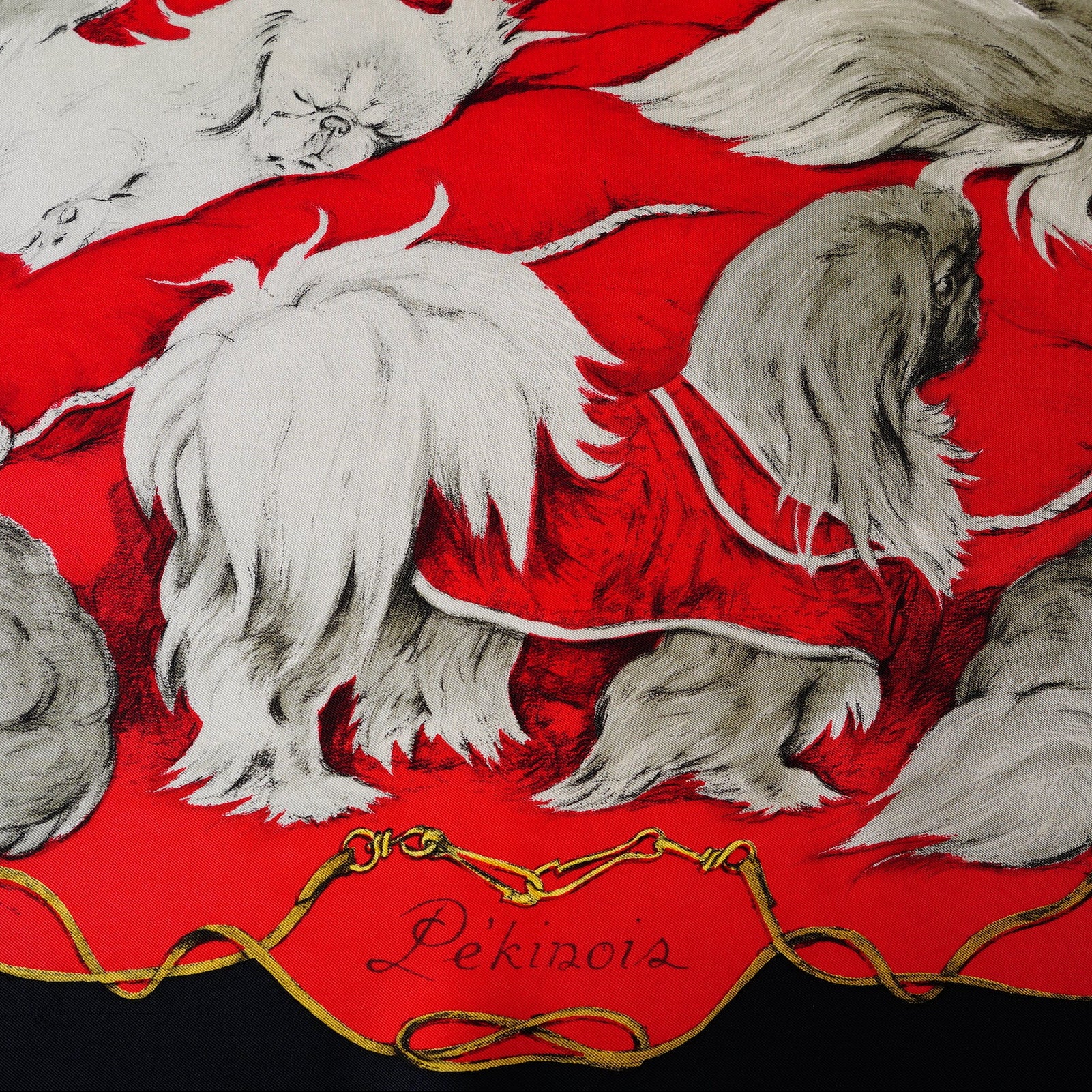 Gros plan sur les chiens Pékinois gris et blancs dessinés par Xavier de Poret sur soie Hermès rouge.