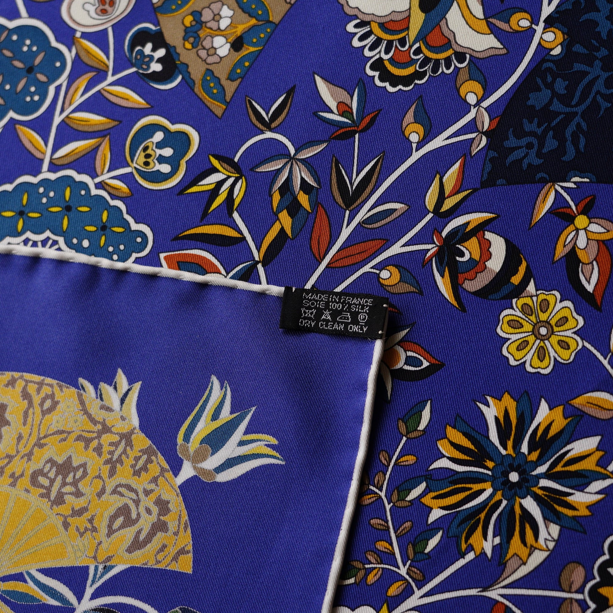 Détail du roulotté contrastant blanc fait main et de l'étiquette de composition sur le foulard Hermès Fleurs et papillons de tissus.