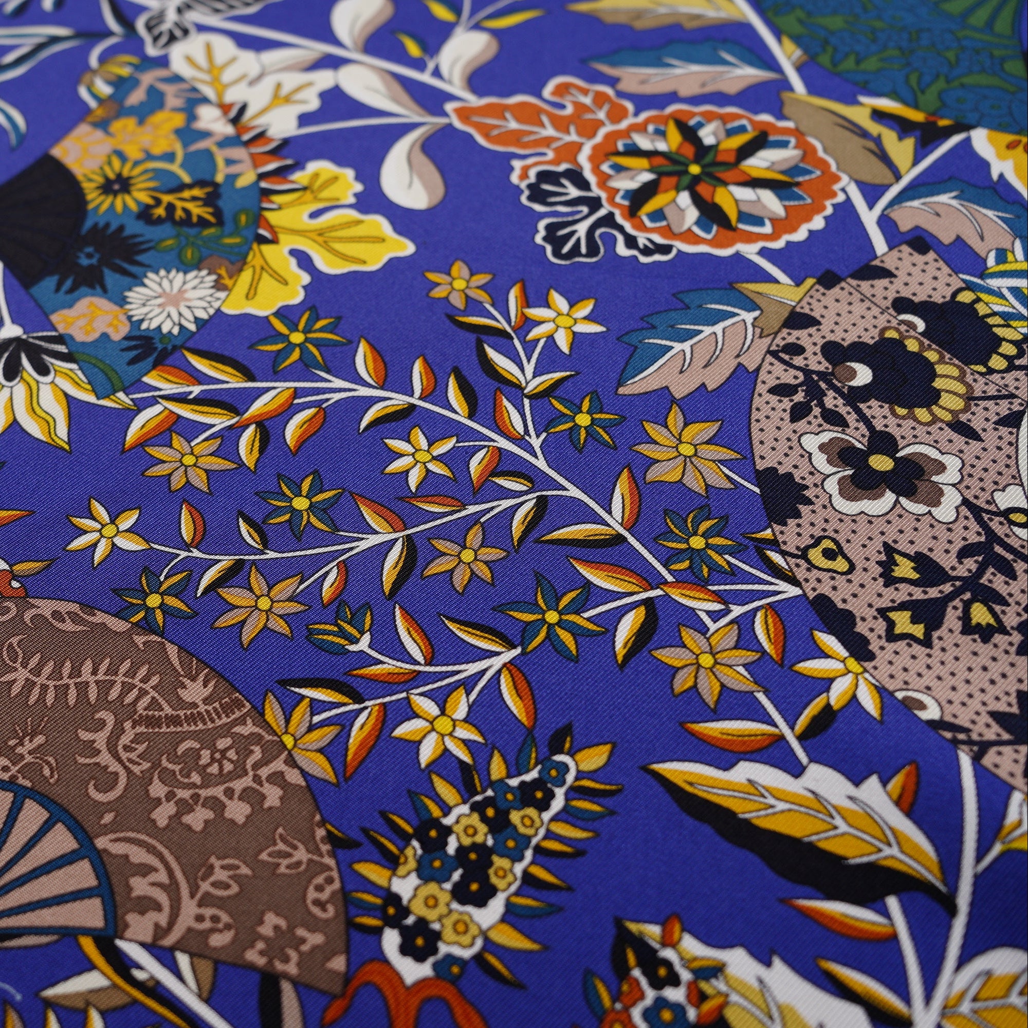 Gros plan sur la richesse des détails floraux et des papillons sur fond bleu roi du carré Hermès Fleurs et papillons de tissus.